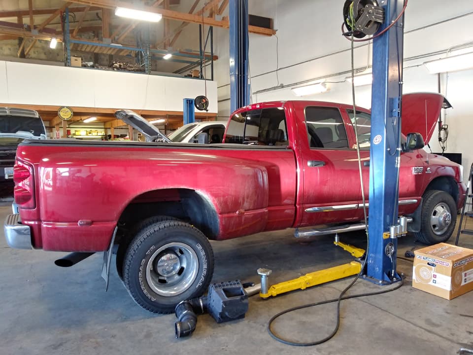 A dark red Dodge Ram dually raised on a two-post lift with its driveshaft out underneath.