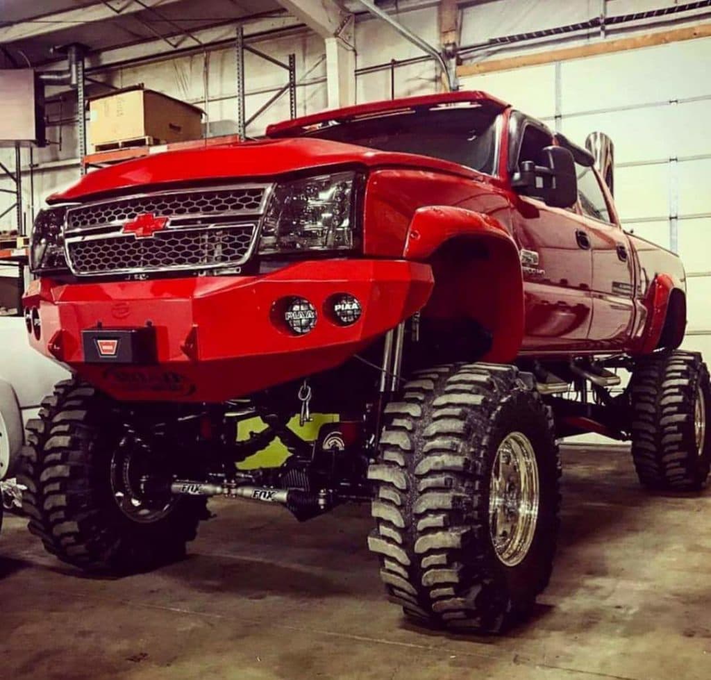 A red lifted Chevrolet dually on oversized mud tyres parked inside a shop bay.