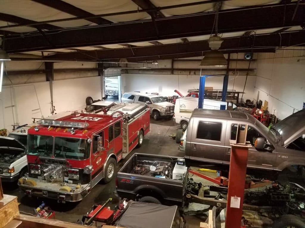 Overhead view of the multi-bay shop with a fire engine, vans and an F-350 on a lift among the work.